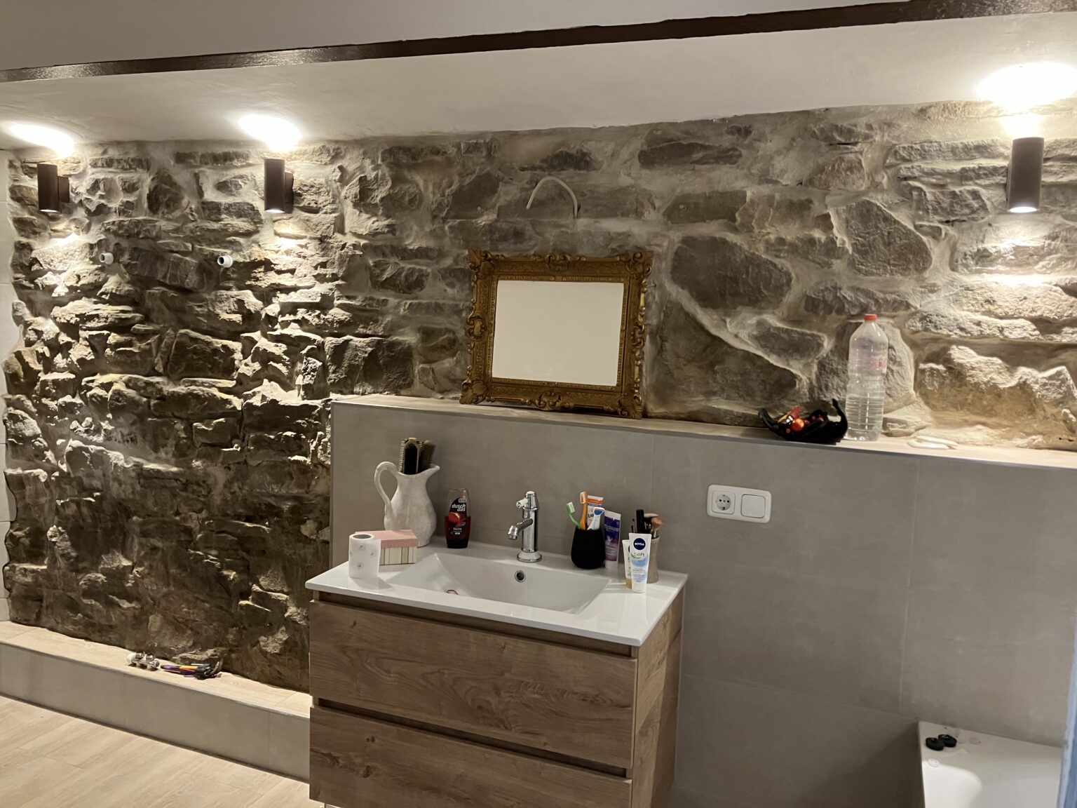 Badezimmer im Gewölbekeller, Natursteinwand, hellen Fliesen und indirekter Beleuchtung