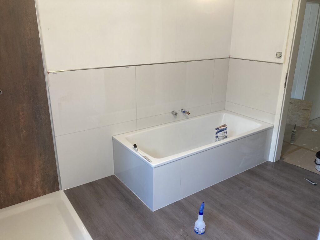 modernes Wannenbad mit großfomatiger, weisser Wandfließe und dunklen Vinylboden in Holzoptik